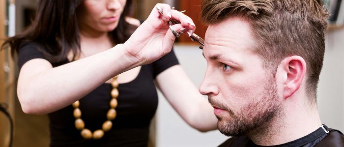 Das Foto zeigt eine Szene beim Friseur: Eine junge Frau schneidet einem junegen Mann die Haare.