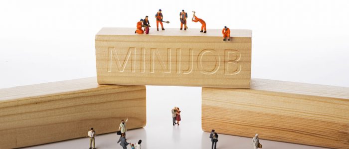 The picture shows three wooden building blocks with workers on top, beneath and in front of them. One building block is inprinted with the word "minijob".