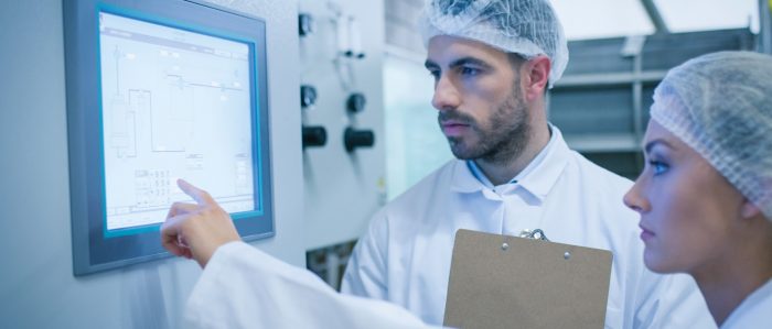Mann und Frau in weißer Arbeitskleidung vor dem Display einer Maschine