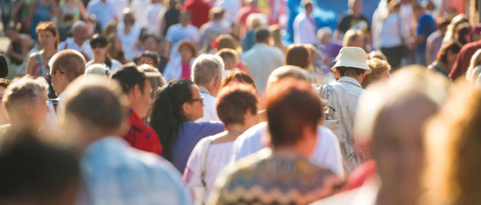 A crowd of people (men, women, young, old, light skin, brown skin) walking, shown from the back.