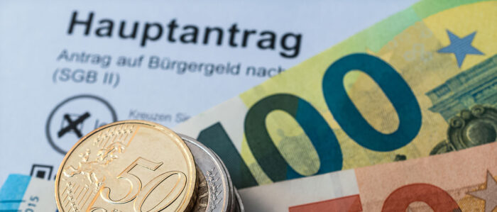 Ein Stapel Münzen und einige Euro-Scheine liegen auf einem Bürgergeld-Antrag.