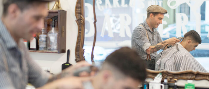 Tätowierter Friseur rasiert in einem Barbershop einem jungen Kunden den Nacken.