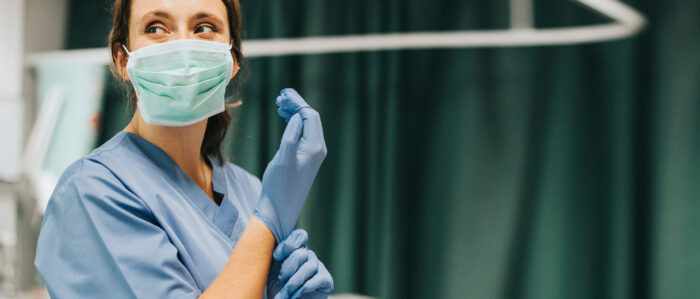 Eine Krankenschwester mit OP-Maske zieht sich Einmalhandschuhe an.