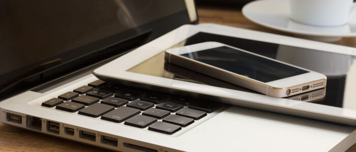 Auf einem Holztisch liegen gestapelt unten ein Laptop, darauf ein Tablet und oben ein Smartphone.