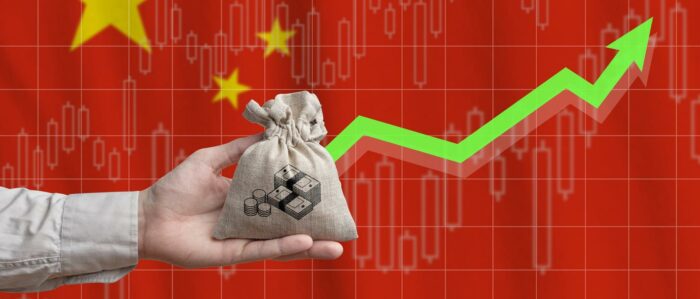 Eine Hand hält einen gefüllten Beutel, auf dem Symbole für Münzen und Banknoten aufgedruckt sind. Im Hintergrund ist die chinesische Flagge zu sehen und ein grüner Pfeil, der nach oben zeigt.