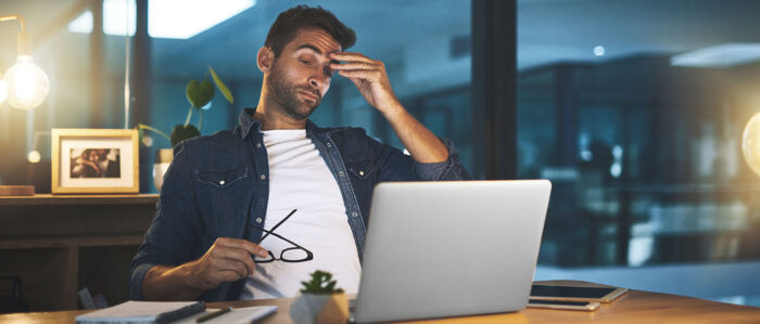 Ein Mann, der nachts im Büro arbeitet, reibt sich müde die Stirn