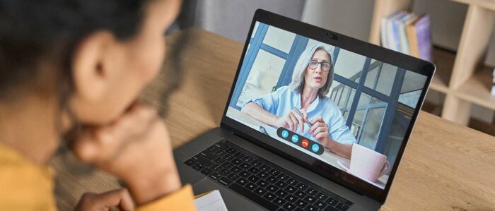Blick über die Schulter auf eine junge Frau, die an ihrem Laptop sitzt und an einer Online-Schulung teilnimmt.