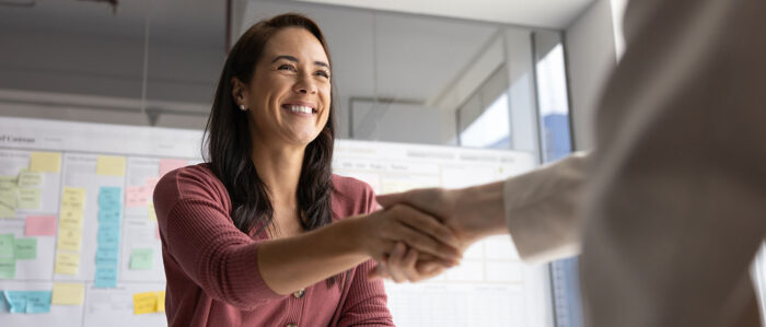 Lächelnde junge Bewerberin schüttelt freudig dem neuen Arbeitgeber die Hand, als sie für die freie Stelle ausgewählt wird.