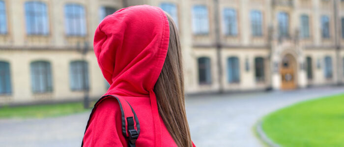 Junges Mädchen dreht sich um und blickt zurück auf ein Universitäts-Gebäude. Foto im Seitenprofil.