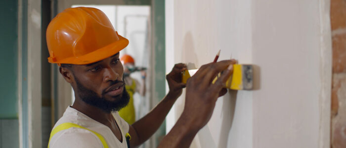 Ein afrikanischer Arbeiter prüft in einem Neubau mit der Wasserwaage ob eine Wand gerade ist.