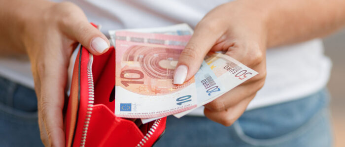 Eine Frau hält in der einen Hand einen roten Geldbeutel, davor in der anderen einen 10-, einen 20- und einen 50-Euro-Schein.