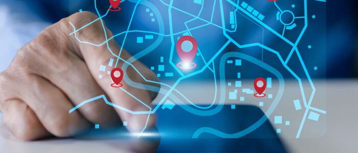 Eine männliche Hand tippt mit dem Zeigefinger auf den Touchscreen eines Notepads. Auf einer virtuellen Ebene davor schwebt ein Stadtplan, auf dem mehrere Orte markiert sind.