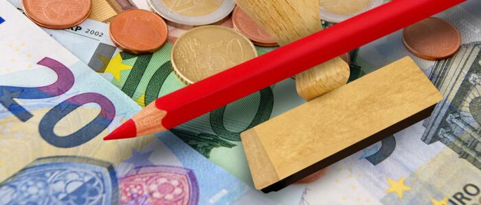 Ein roter Stift und ein Stempel liegen auf verschiedenen Euroscheinen und -münzen.