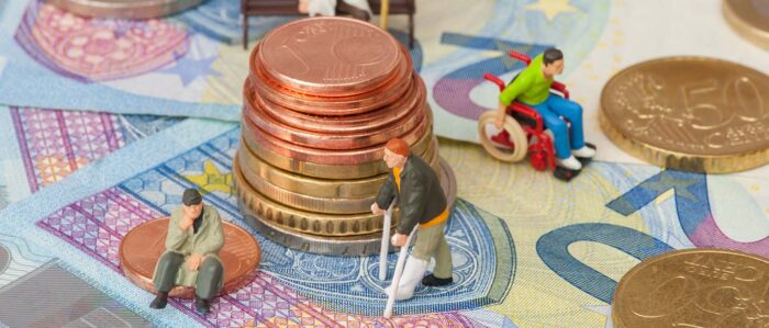 Miniaturfiguren von älteren Menschen oder solchen mit körperlichen Beeinträchtigungen auf einer Landschaft aus Geldscheinen und Münzen.