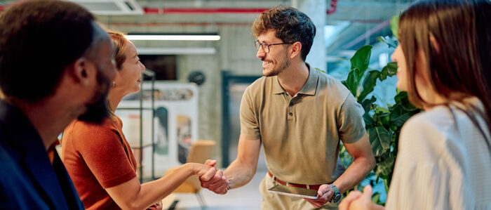 Ein Business-Team begrüßt einen neuen Mitarbeiter mit einem Händedruck in einem modernen Büro.