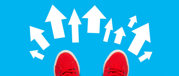 Blick von oben auf rote Turnschuhe, die auf einem hellblauen Hintergrund mit mehreren weißen Pfeilen stehen. Die Pfeile zeigen in verschiedenen Richtungen.