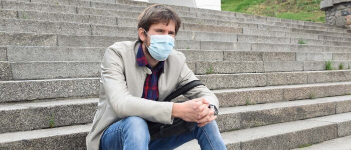 Ein Mann mit OP-Maske sitzt alleine im Freien auf einer breiten Treppe.