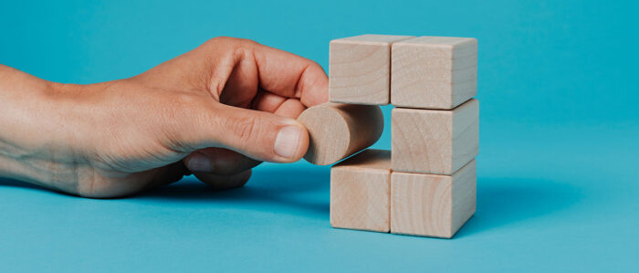 Eine Hand schiebt einen runden Bauklotz an eine freie Stelle in einem Turm aus eckigen Bauklötzen.