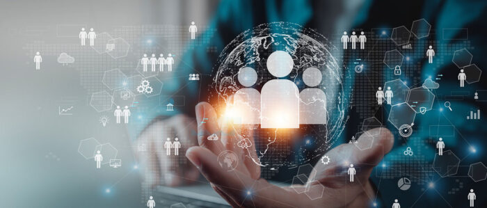 Leuchtende Personen-Symbole schweben über der geöffneten Hand eines Mannes, der vor einem Laptop sitzt.