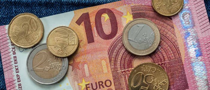 Mindestlohnerhöhung: 13,90 Euro, ein 10-Euro-Schein und mehrere Münzen liegen auf einer Jeanshose.