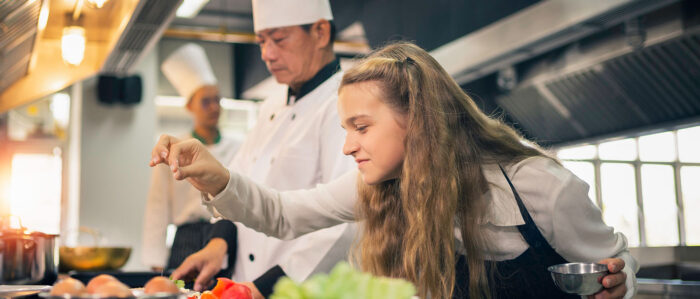 Koch und weiblicher Lehrling bei der Arbeit in einer Großküche.