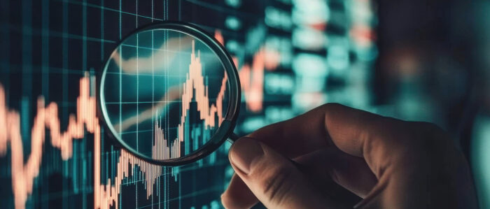 Hand, die eine Lupe auf ein Diagramm auf einem Bildschirm hält.