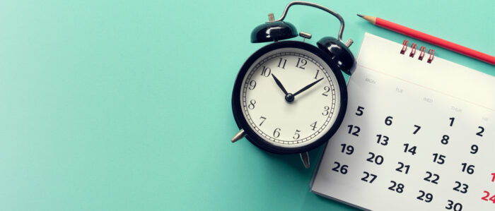 Wecker und Kalender und Bleistift auf türkisfarbenem Hintergrund.