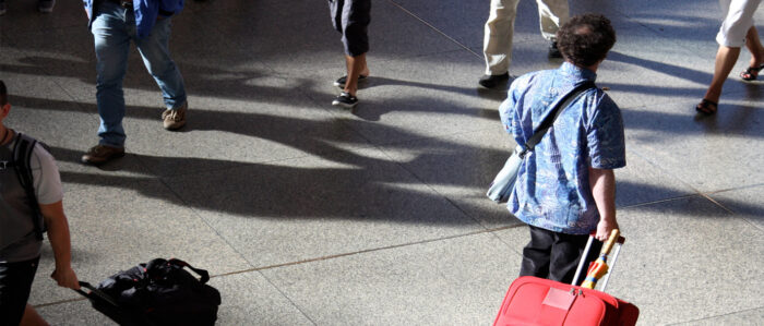 Mann mit Rollkoffer von hinten.