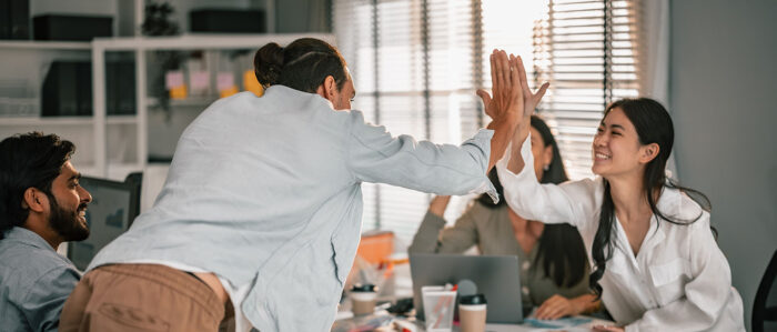 Zwei lachende Kollegen im Büro, eine Frau und ein Mann, klatschen mit einem „High five“ ab, um der Zufriedenheit über einen Erfolg Ausdruck zu verleihen.